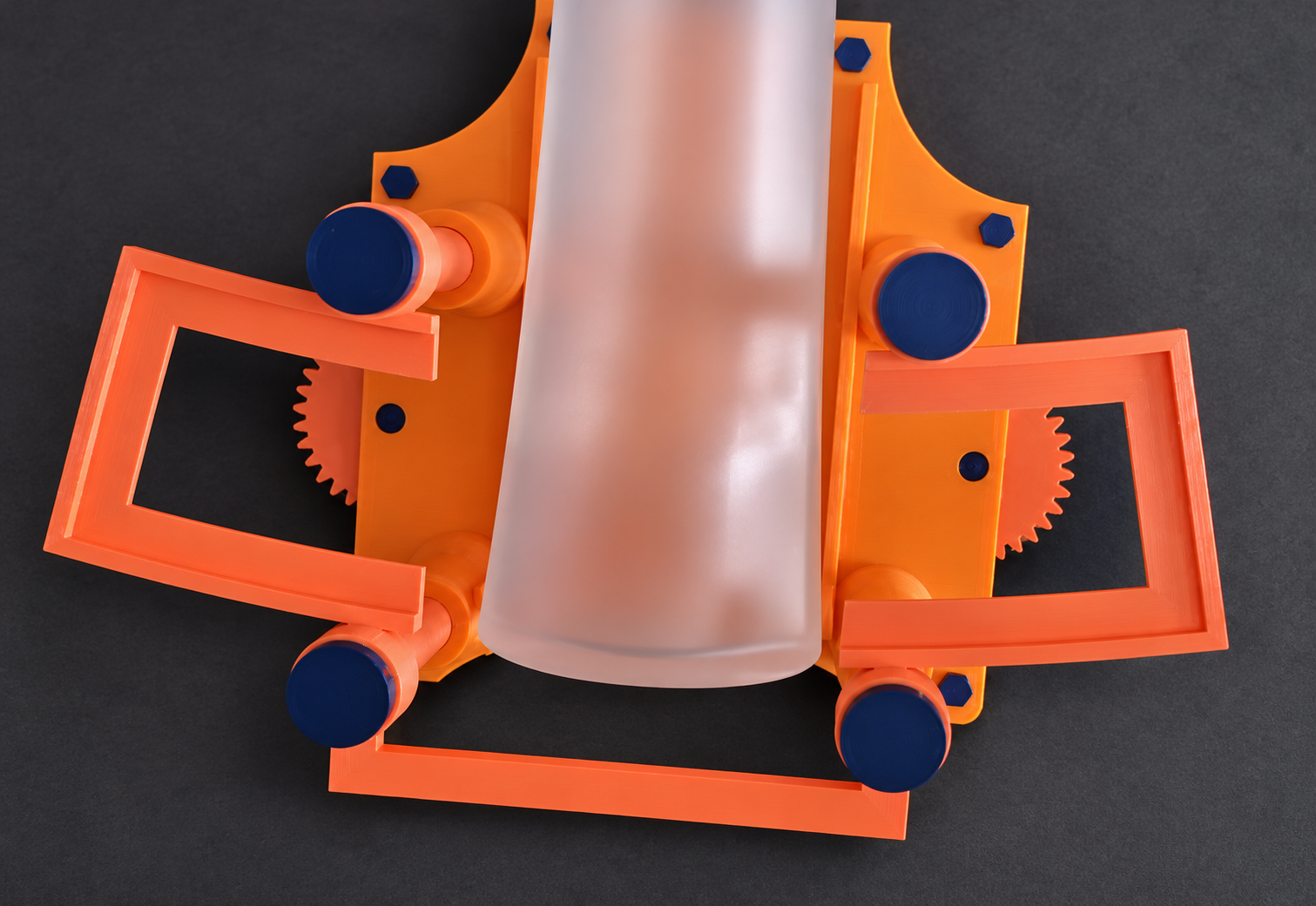 Orange 3D printed bottle labelling jig with open side guides, blue adjustment pads and a frosted bottle on a charcoal background.