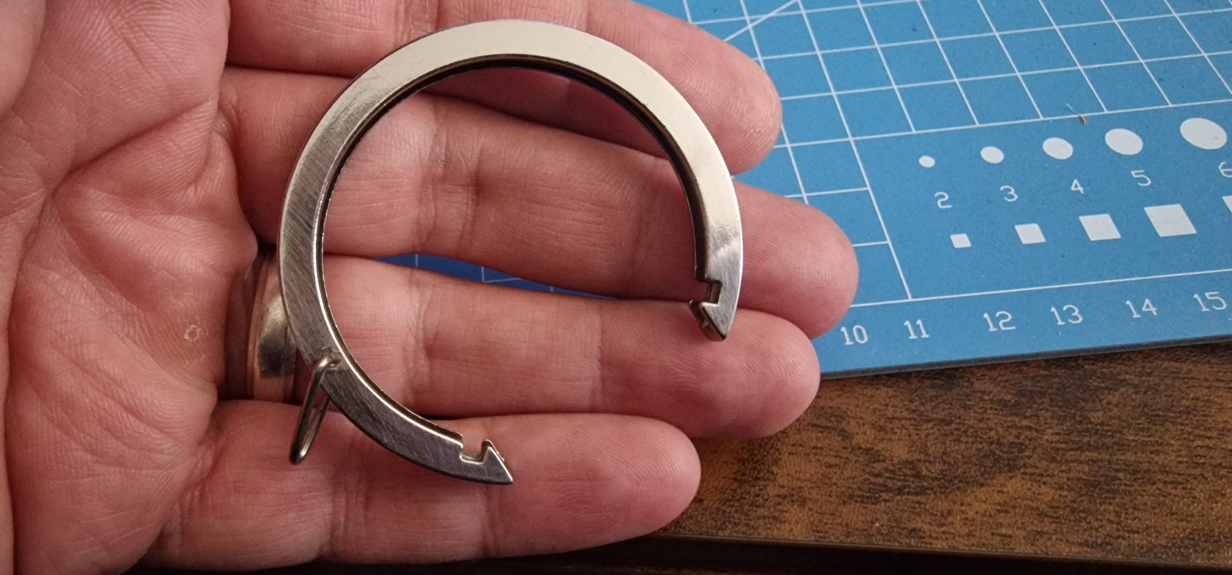 A C-shaped metal curtain ring held in a hand, showing its inner channel and notched ends.