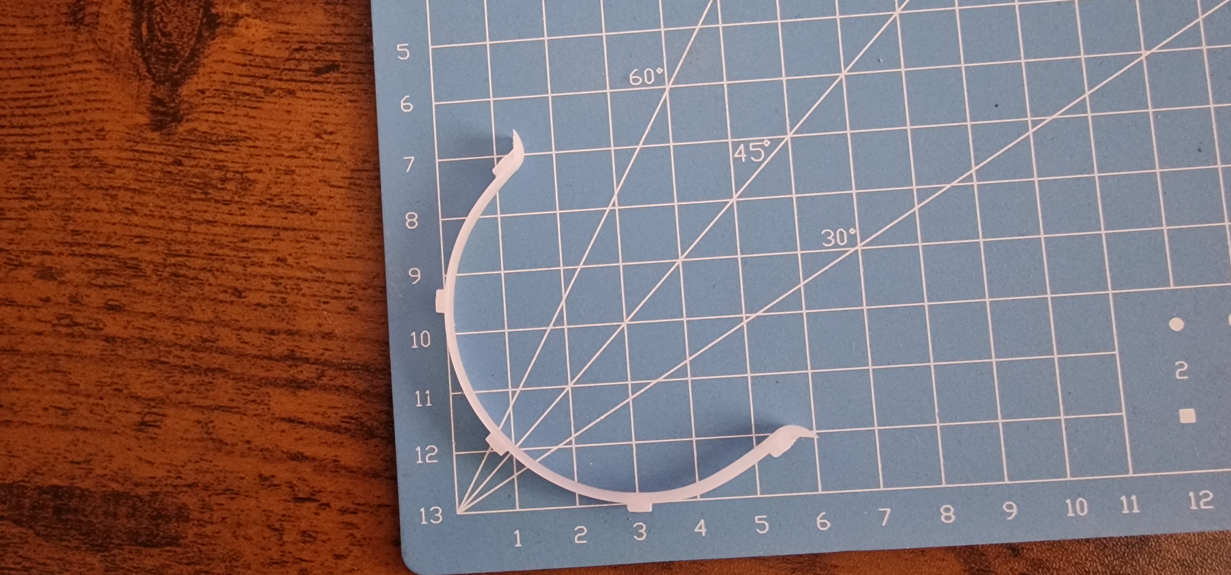 A thin white curved curtain ring insert with small locating tabs on a blue gridded cutting mat.